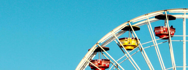 Part of a ferris wheel with red and yellow cabins against a clear blue sky