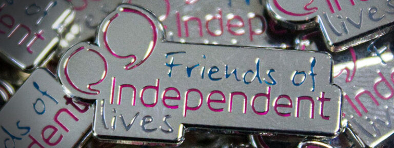 Close-up of "Friends of Independent Lives" pin badges with reflective silver and purple accents