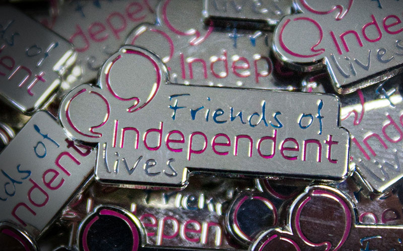 Close-up of "Friends of Independent Lives" pin badges with reflective silver and purple accents