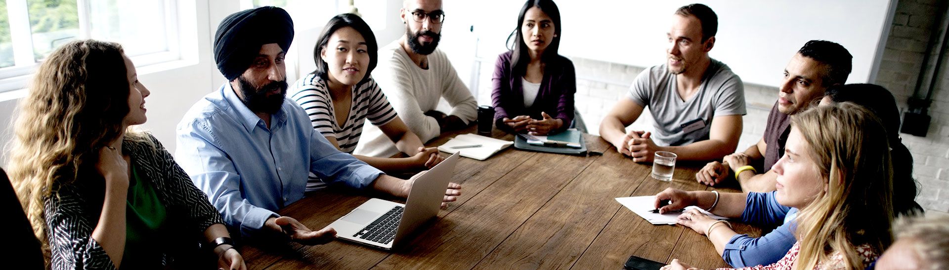 A multicultural team engaged in discussion around a wooden table in a bright office.