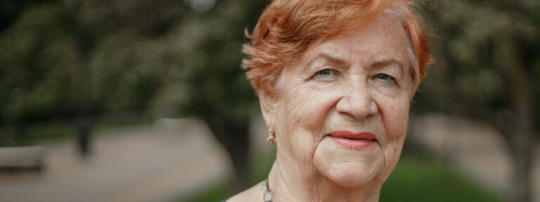 Elderly lady with red hair and a wise gaze in a park setting.