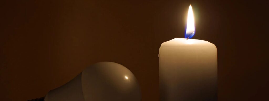 white candle with a bright flame next to an unlit light bulb