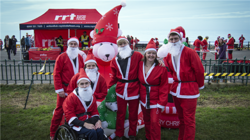 Group of volunteers dressed as Santa Claus at a charity event by the seaside.