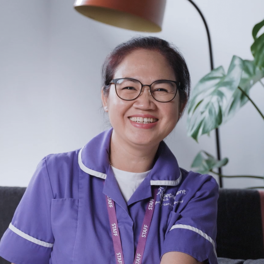Smiling healthcare worker in purple uniform with staff lanyard