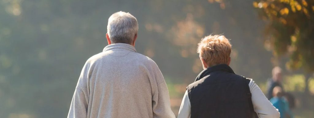 An older couple enjoying a leisurely walk together in a sunlit park.