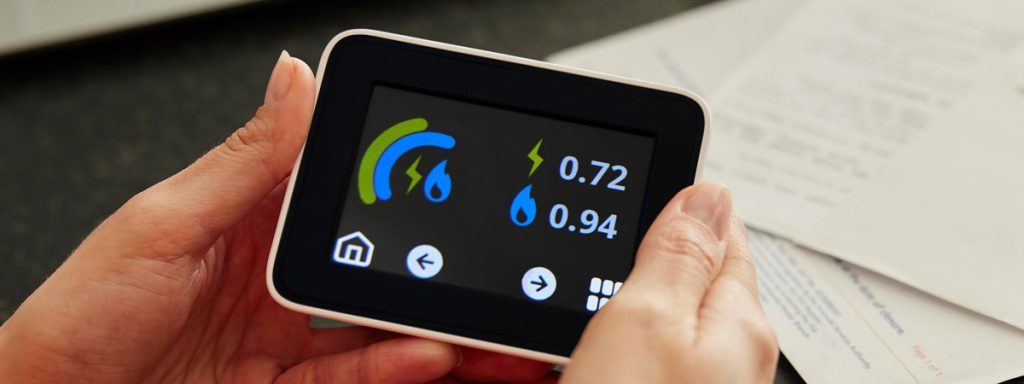 Close-up of a hand holding a modern digital utility meter displaying water and electricity usage.