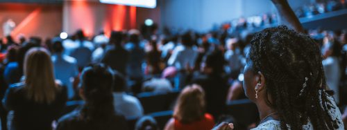 An audience member actively participates in a conference, raising a hand among the crowd.