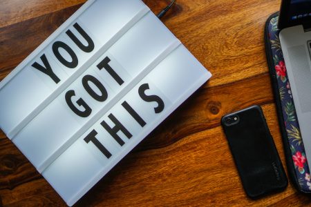 Lightbox with the words "YOU GOT THIS" on a wooden surface next to a smartphone and a laptop case.