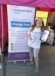 Joyful young volunteer holding a certificate and mug at Independent Lives event.