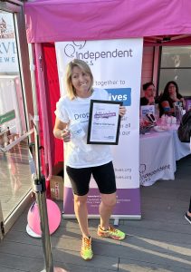 Woman smiling while holding a certificate and a mug in front of a charity event banner.