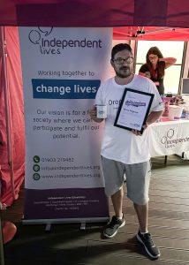 Man holding a certificate and a mug in front of a charity's promotional banner at an event