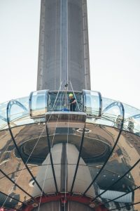 A person in safety gear is seen through the glass floor of an observation deck high above the ground.