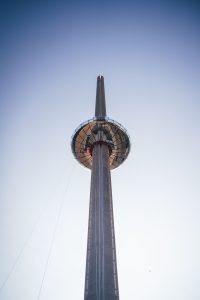 Upward view of a tall observation tower with a glass-bottomed deck and a clear sky in the background.