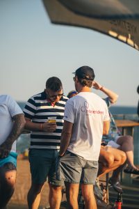 Two men engaged in conversation at an outdoor event, one wearing a T-shirt with a charity logo.