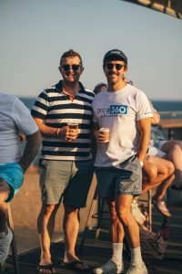 Two smiling men holding drinks and enjoying a social event outdoors.
