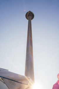 Sunlight flares around the base of a towering observation tower with a prominent viewing deck.