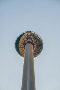 A tall observation tower with a large glass viewing platform against a bright blue sky.