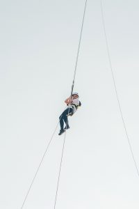 A person in a white helmet and harness abseiling with a clear sky in the background.