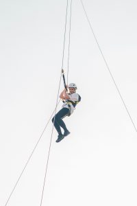 A person abseiling down with ropes against a clear sky background.