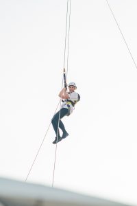A smiling person abseiling down a building, secured with ropes and safety gear.