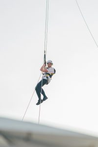 A person in safety gear suspended on a rope during an abseiling activity.