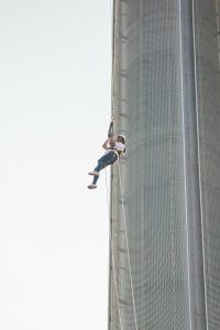 An individual in a helmet and harness is rappelling down the side of a modern skyscraper.
