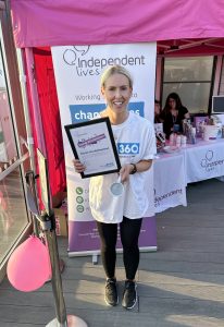 A smiling woman stands holding a congratulatory certificate and a mug in front of an Independent Lives banner.