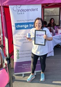 A joyful woman holding a certificate and a mug in front of an Independent Lives banner.