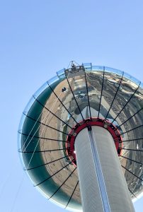 Close-up view of a thrill-seeker abseiling down the i360 glass observation tower with the Brighton cityscape reflected in its surface