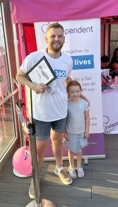 Man holding a certificate and a young girl smiling beside an Independent Lives charity banner.
