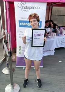 A woman with a certificate and a mug in front of an Independent Lives charity banner.