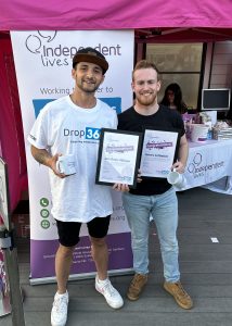 Two men holding certificates and a mug in front of a charity event banner