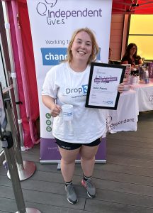 Woman holding a certificate and mug, smiling, in front of a charity event backdrop.