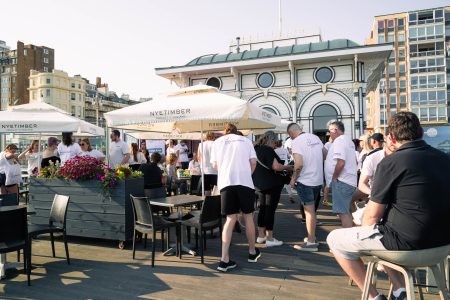 Community gathering of Independent Lives volunteers on a sunny deck with parasols, engaging in conversation and networking.