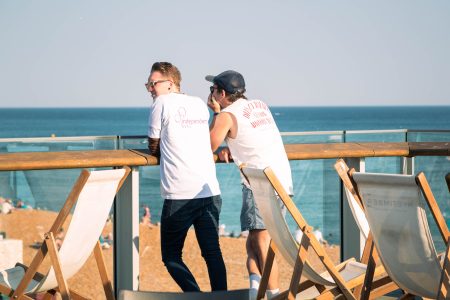 Two volunteers in white shirts with the Independent Lives logo discussing over a seaside railing.