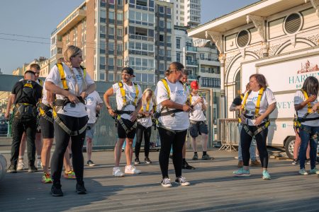 Group of people in white t-shirts and safety harnesses preparing for an outdoor abseiling event.