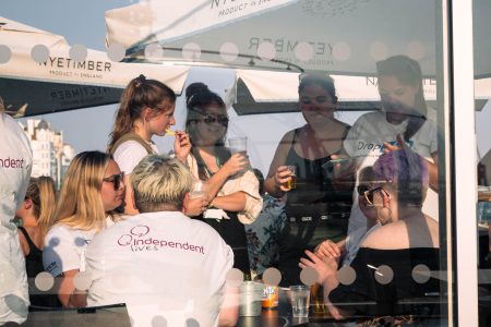 Event attendees enjoy a gathering for Independent Lives, engaging in conversations behind a glass pane.