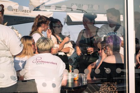 Event attendees enjoy a gathering for Independent Lives, engaging in conversations behind a glass pane.