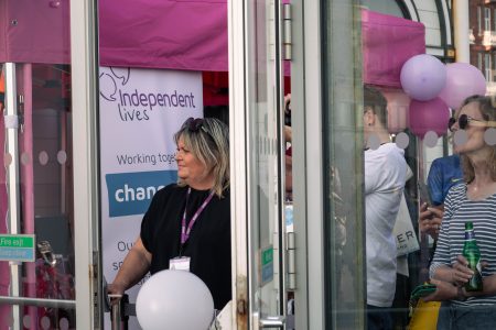 A woman from Independent Lives charity smiles while standing by a door at an outdoor fundraising event.