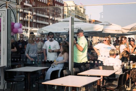 Guests mingle and enjoy a social event in a coastal setting, with a woman in the foreground sharing a laugh.