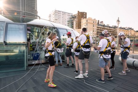 Abseiling participants prepare for a charity event on an outdoor platform with urban buildings in the background.