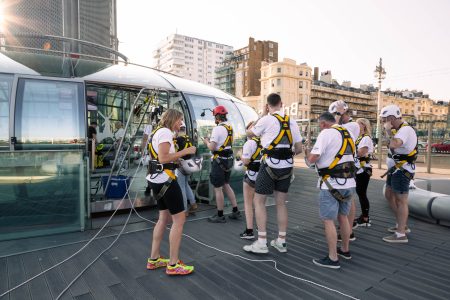 Abseiling participants prepare for a charity event on an outdoor platform with urban buildings in the background.