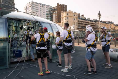 Abseiling participants prepare for a charity event on an outdoor platform with urban buildings in the background.