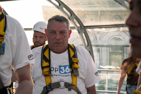 A focused participant in abseil gear listens intently amidst fellow abseilers at a charity event.