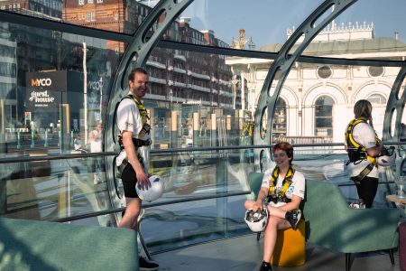 Charity abseil participants share a light-hearted moment inside a glass structure with urban architecture in view.