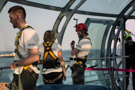 Abseil participants with safety gear and helmets inside a glass structure preparing for a charity event.