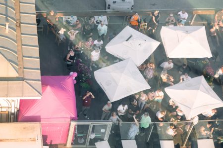 Bird's-eye view of spectators gathered under parasols at an outdoor event, viewed from above.