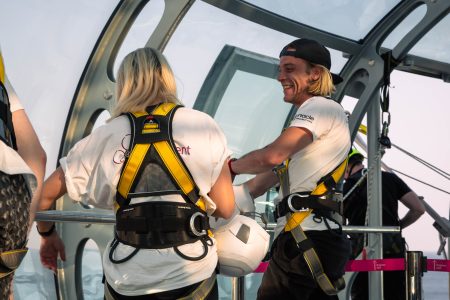 Smiling charity abseil participants in safety gear engage in conversation before their descent at a high-altitude event.