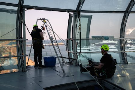 Two abseiling instructors check equipment on a high-altitude platform overlooking the ocean.