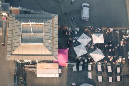 Bird's-eye view of spectators gathered under parasols at an outdoor event, viewed from above.